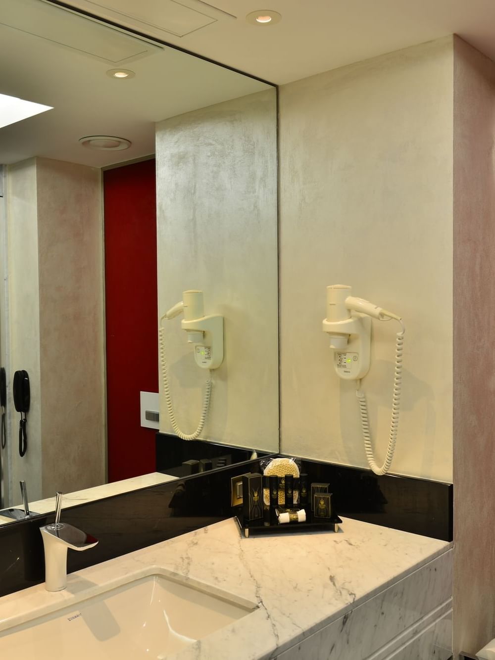 Marble sink by a vibrant red wall under a large mirror in Junior Suite at Warwick Ankara