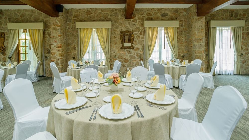 Salón Virreinal with stone walls, round dining tables, and white chair covers at Quinta Real Guadalajara