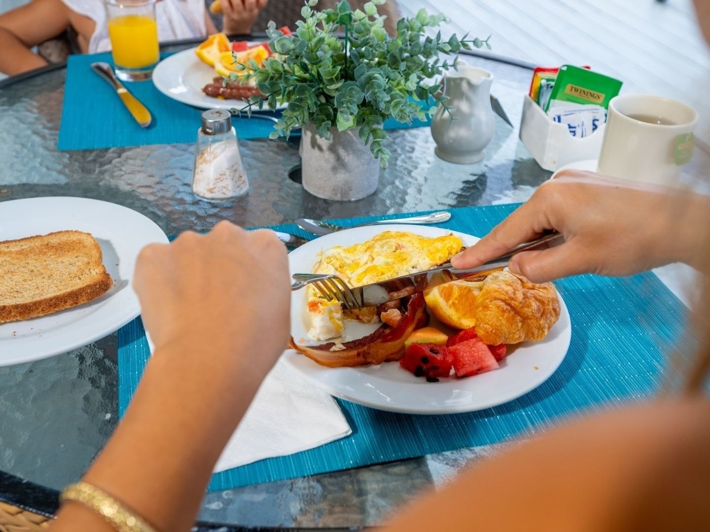 Person eating a breakfast plate of eggs, bacon, toast, and fruit at Savannah Beach Hotel.