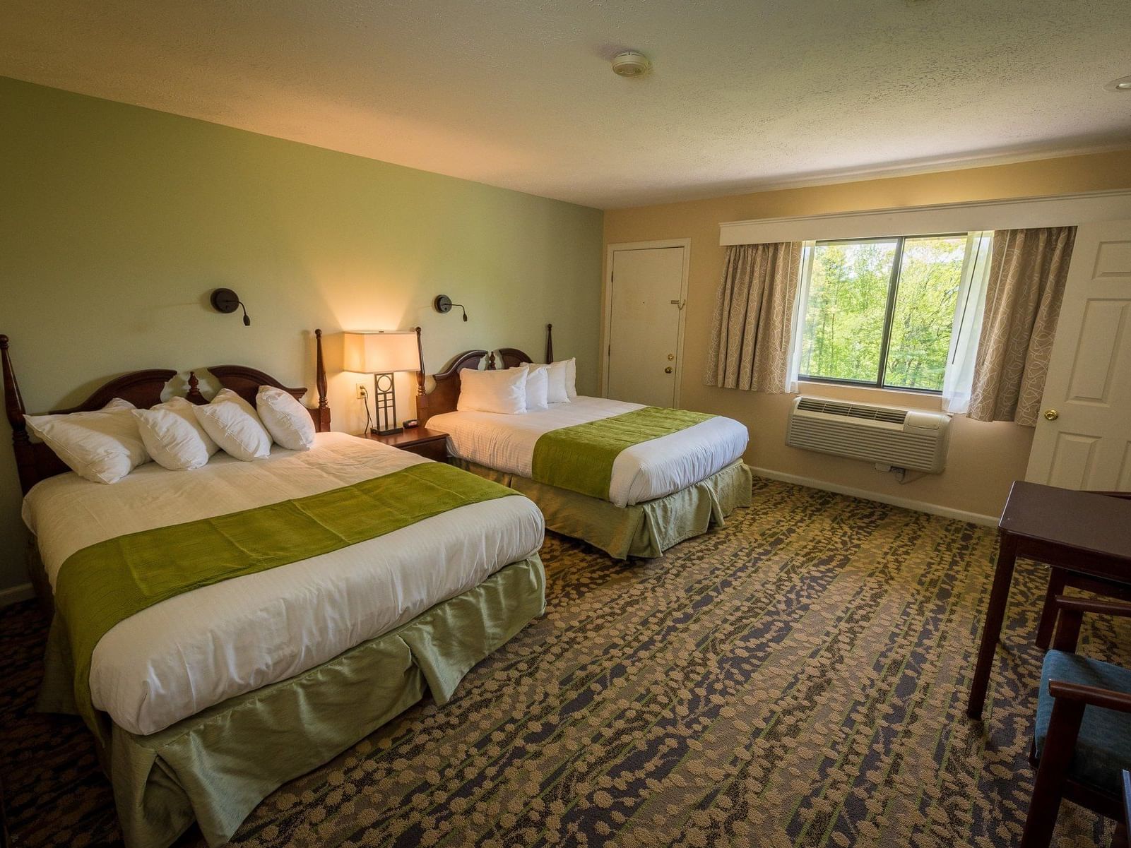 Two queen beds with green covers and pillows in a room with a mountain view at Fox Ridge Resort in Conway.