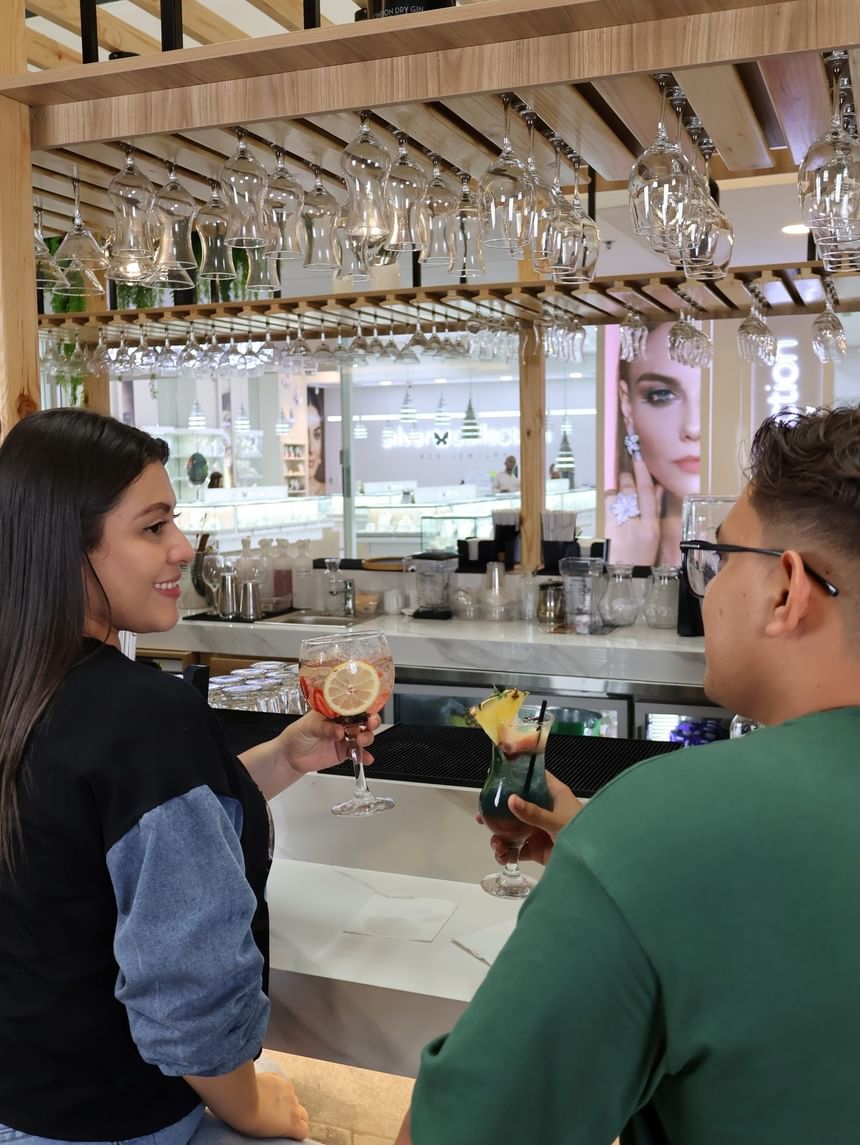 Hombre y mujer con cócteles en un bar moderno bajo copas de vino colgantes en Megapolis Hotel Panama