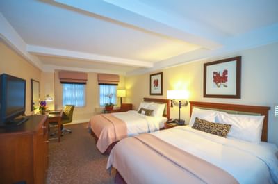 A deluxe room with two beds, a desk, TV, two framed pictures, and carpeted floor.