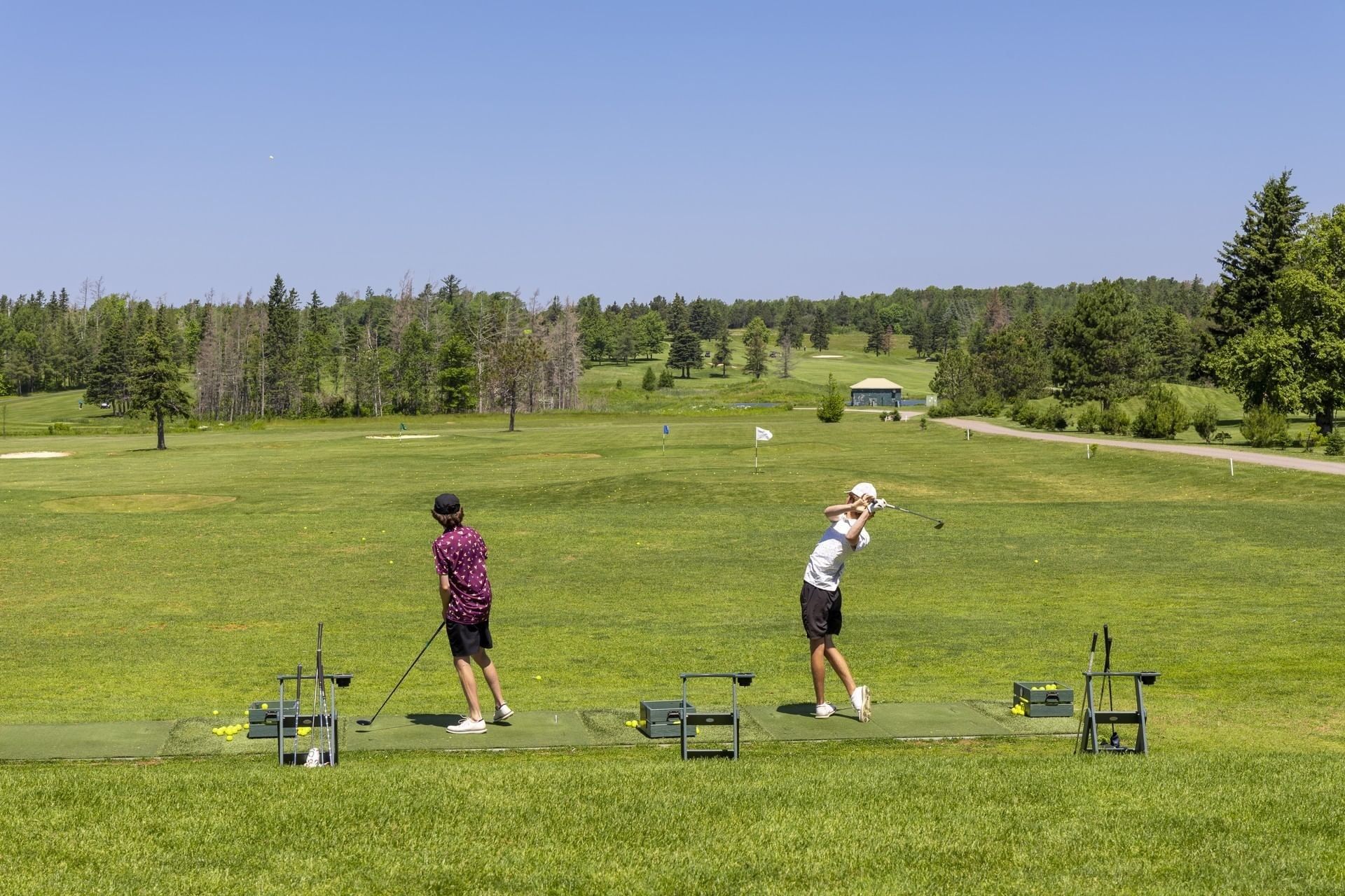 Two people practicing swings on a range at Crowbush Golf Resort, part of Rodd Crowbush Golf & Beach Resort