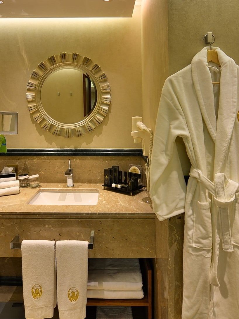 White bathrobe on a hook by a marble vanity under a round sunburst mirror in Ankara Suite with Terrace at Warwick Ankara