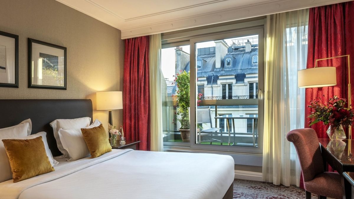 Neat bed by a sliding glass door under red curtains in Deluxe Room with Terrace at Warwick Paris Champs Elysées