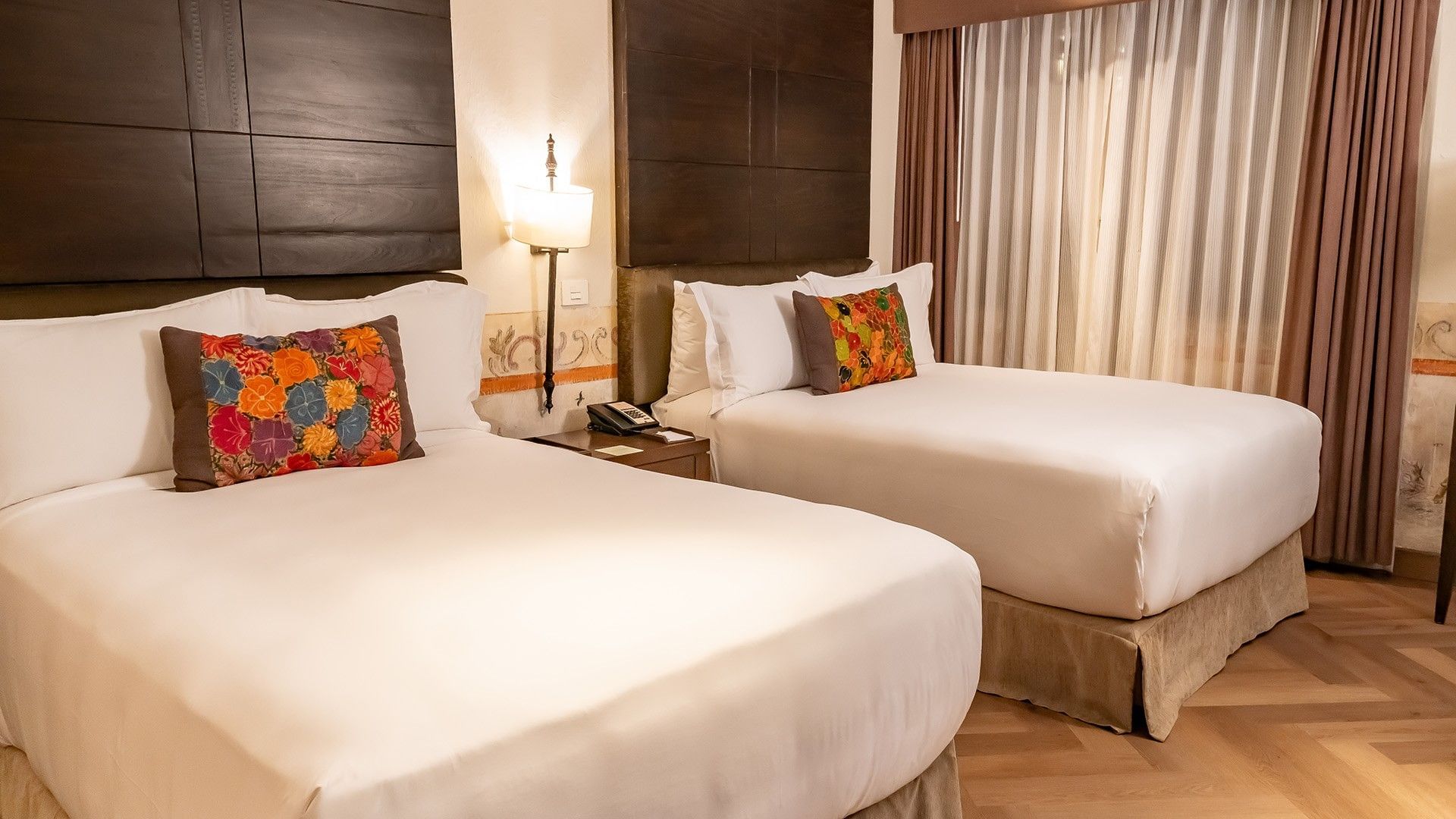 Two Double Novicia with two beds, colorful floral pillows, dark wood panels, and warm wall sconces at Quinta Real Puebla
