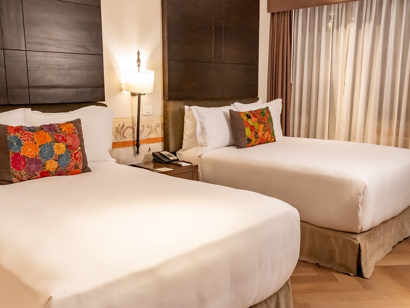 Two Double Novicia with two beds, colorful floral pillows, dark wood panels, and warm wall sconces at Quinta Real Puebla