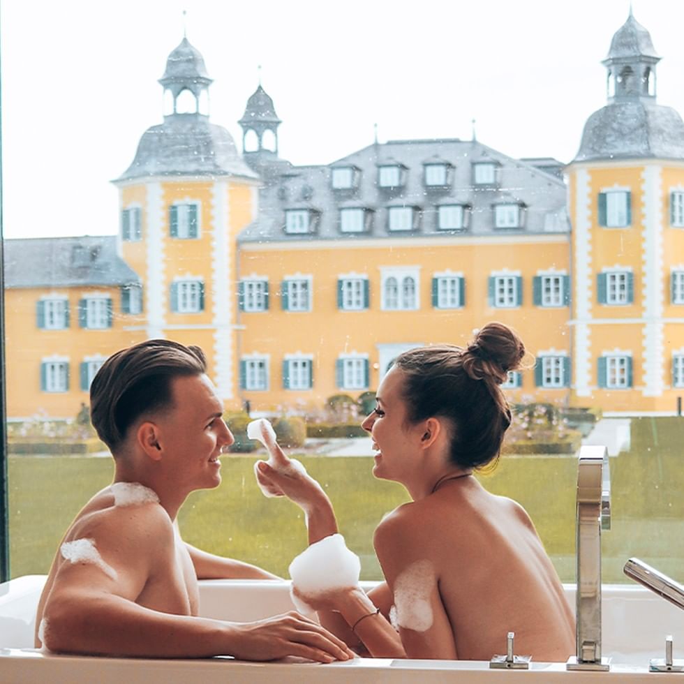 Due persone si rilassano in una vasca da bagno con vista su un castello.