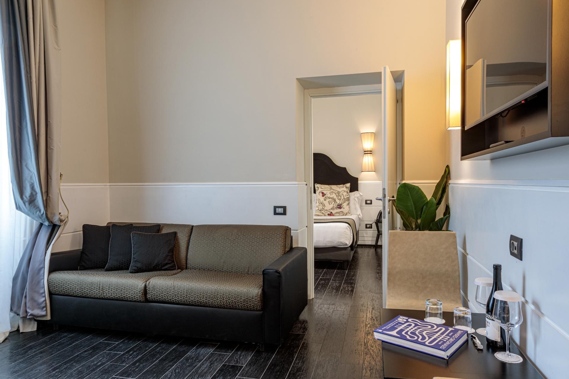 Modern Family Room with a stylish sofa, bedroom view, TV, mini-bar, and elegant decor at The Independent Suites