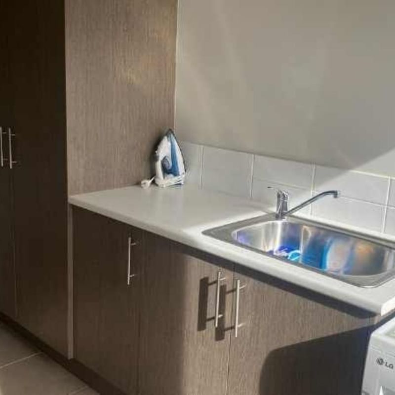 Clean laundry room with washing machine, sink, and ironing board at La Trobe University Regional Housing – Mildura.