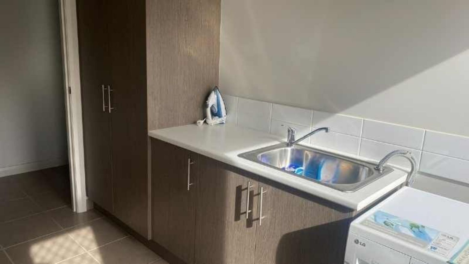 Clean laundry room with washing machine, sink, and ironing board at La Trobe University Regional Housing – Mildura.