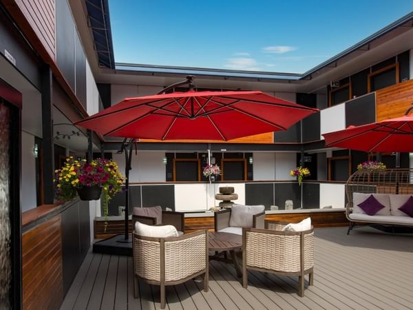 Outdoor patio with red umbrellas, wicker chairs and a bench under a clear sky.