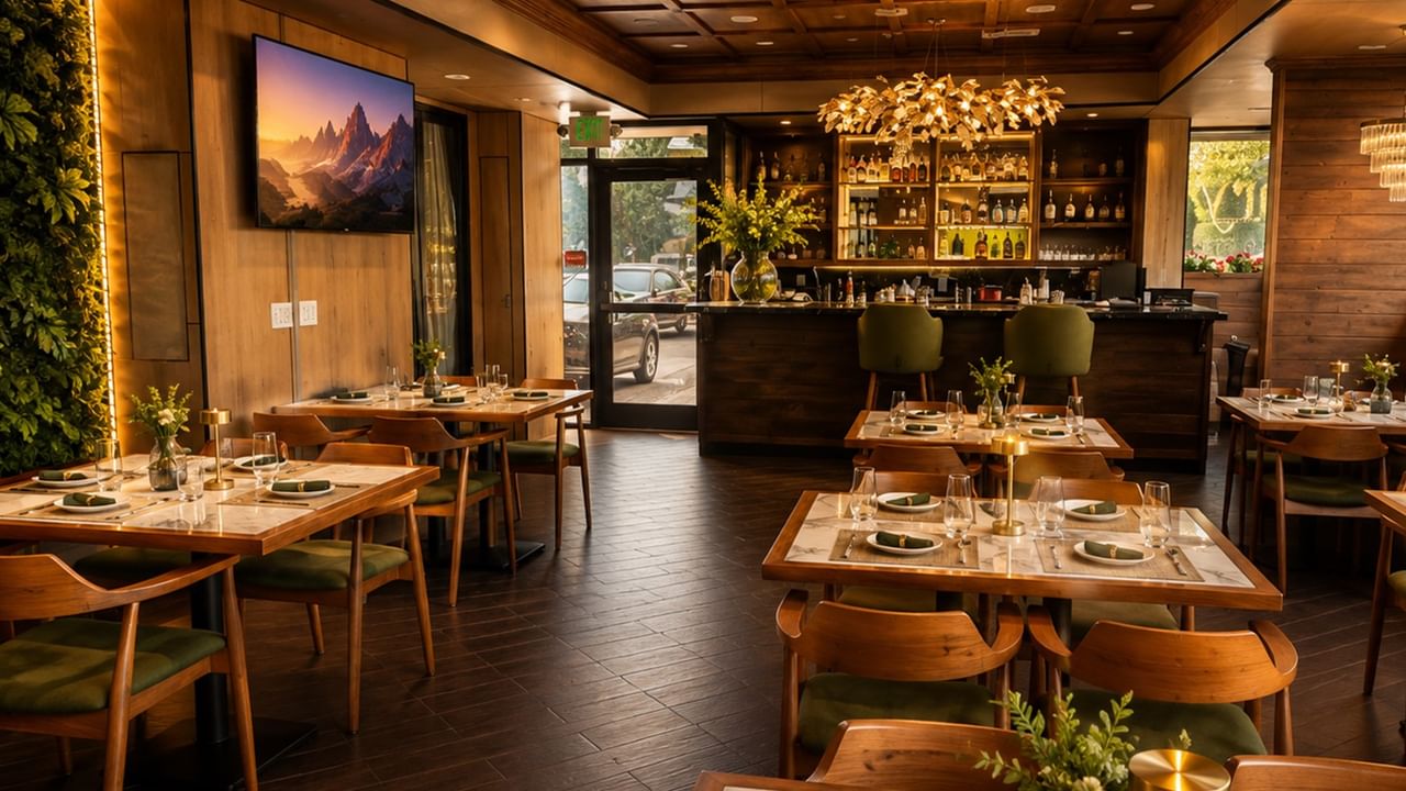 Arya restaurant interior with wooden tables, elegant lighting, and a bar at Safari Inn, a Coast Hotel in Burbank