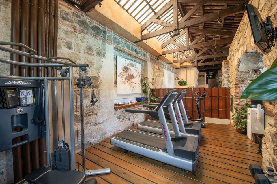 Gimnasio con paredes de ladrillo visto, techo de madera y varias máquinas de ejercicio en Casa Santo Domingo