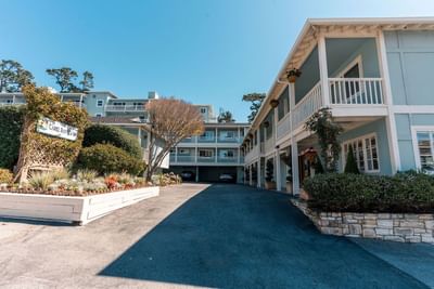 The sunny exterior view of the light blue multi-story hotel with a paved driveway and lush landscaping at Carmel Bay View Inn