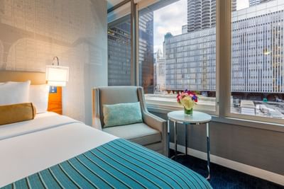 Bed & a chair by a window facing the city at Kinzie Hotel room