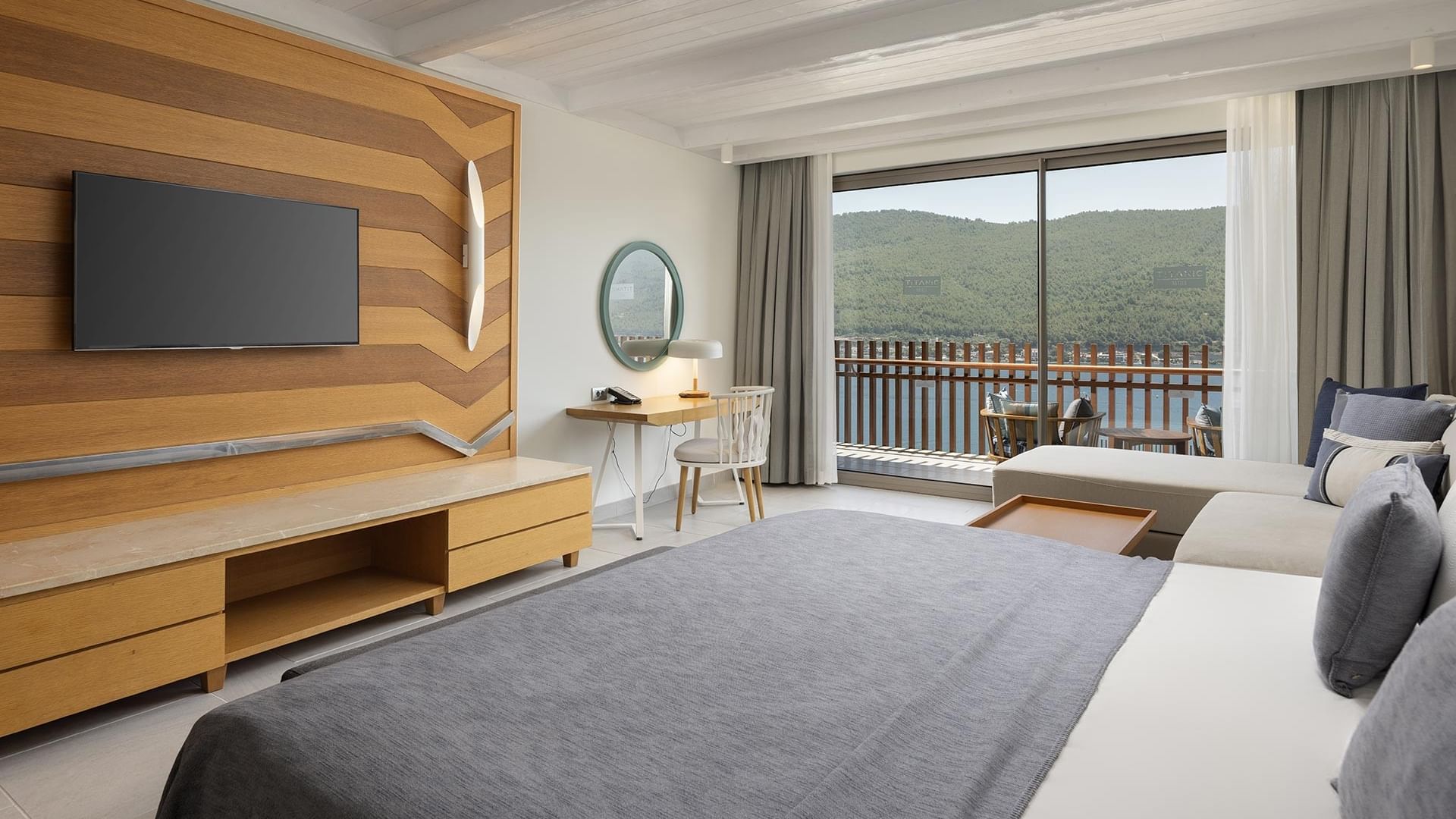 Superior Sea View Room with a large bed, desk, TV, and balcony overlooking greenery and sea.