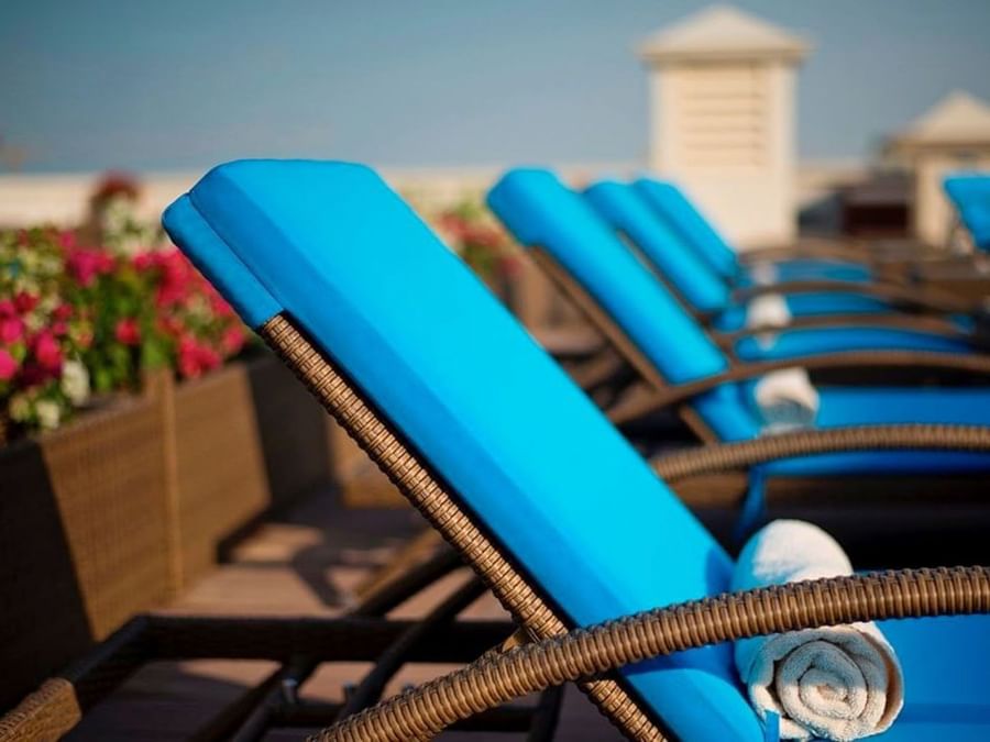 Bright blue pool loungers by rolled towels under the tropical sun on the rooftop deck at Warwick Doha Hotel