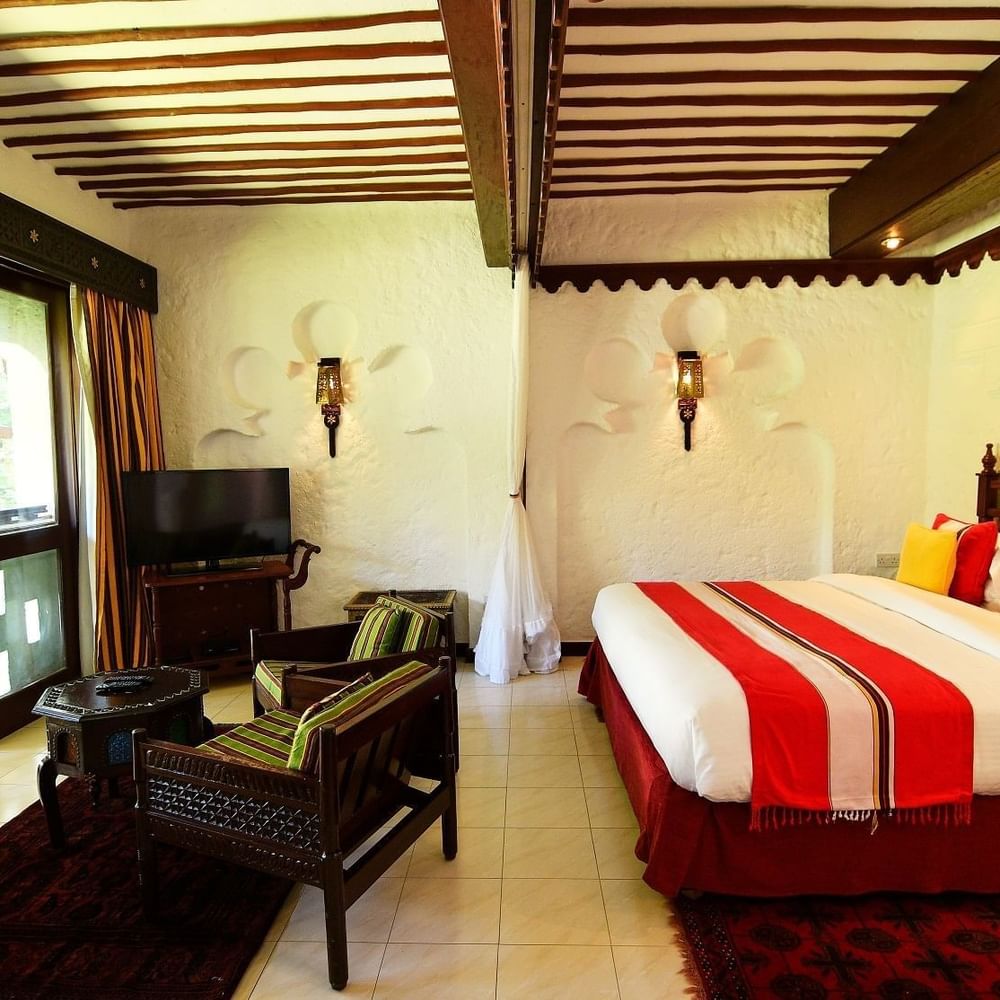 Elegant Garden Suite interior with a cozy bed, chairs, and a television at Serena Beach Resort & Spa in Mombasa.