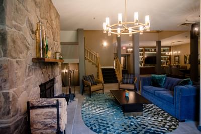 Lobby lounge with blue sofa and armchairs arranged around a stone fireplace and rug at La Tourelle Hotel and Spa