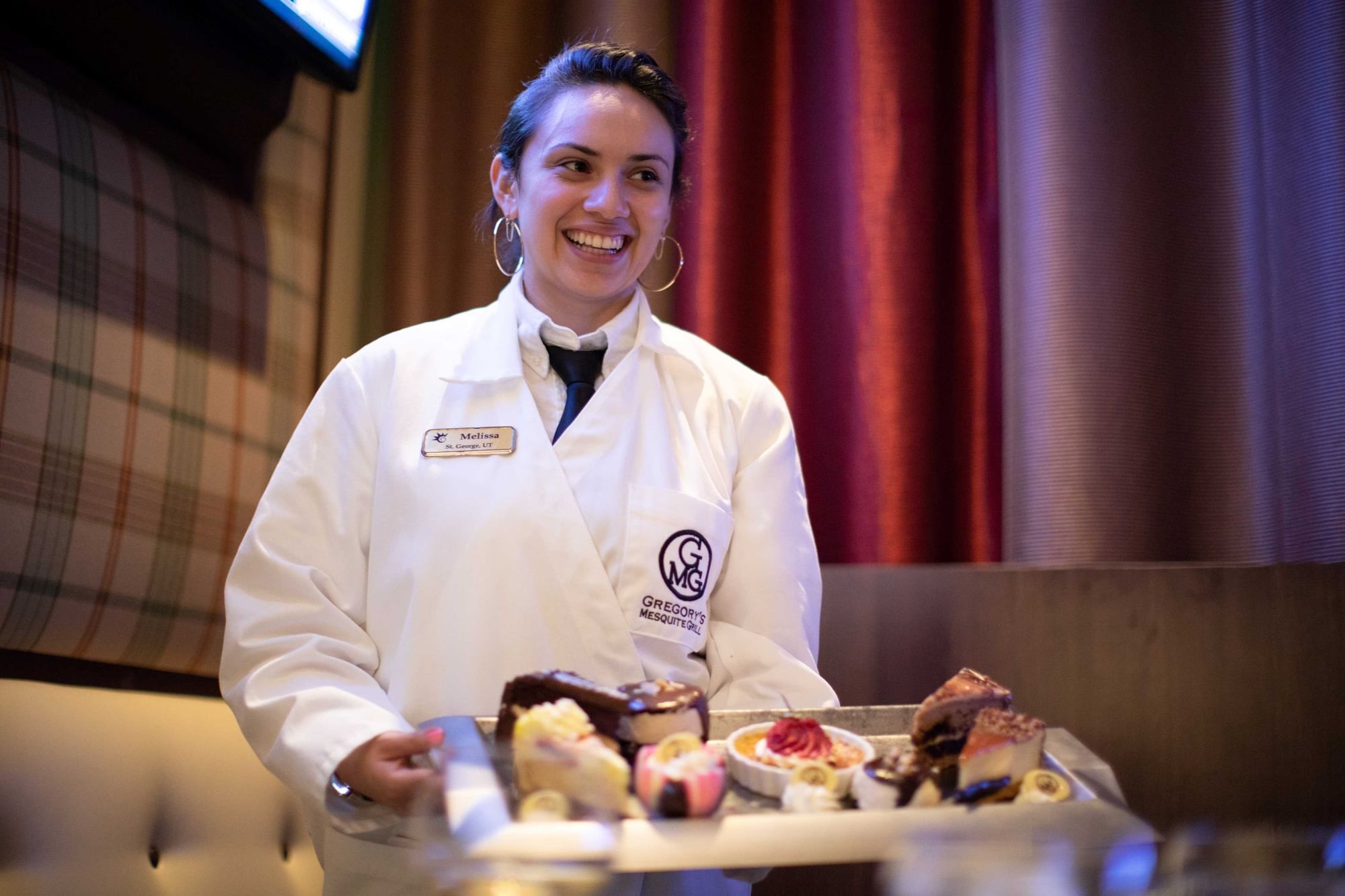 Smiling server carrying a tray of dessert samples in a white jacket near Gregory\'s Mesquite Grill at Eureka Casino Resort
