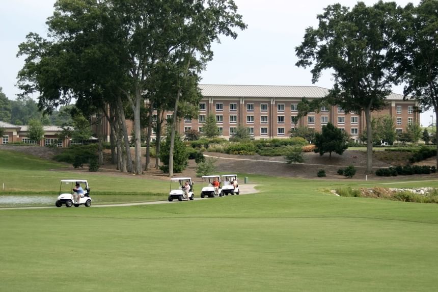 Golf carts crossing a green fairway before a big brick inn among oak trees at Clemson University Conference Center & Inn