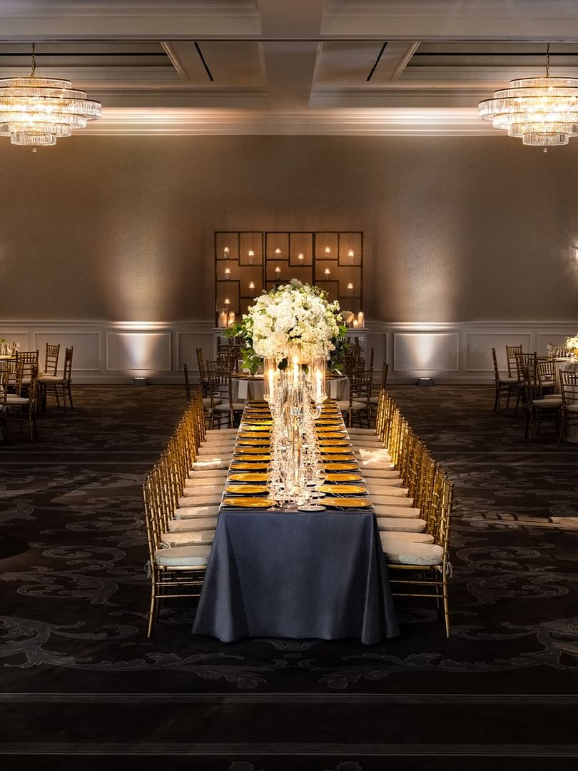 Long banquet table by gold chairs under tiered crystal chandeliers in Turtle Creek Ballroom at Warwick Melrose Dallas