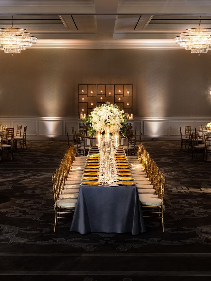 Long banquet table by gold chairs under tiered crystal chandeliers in Turtle Creek Ballroom at Warwick Melrose Dallas