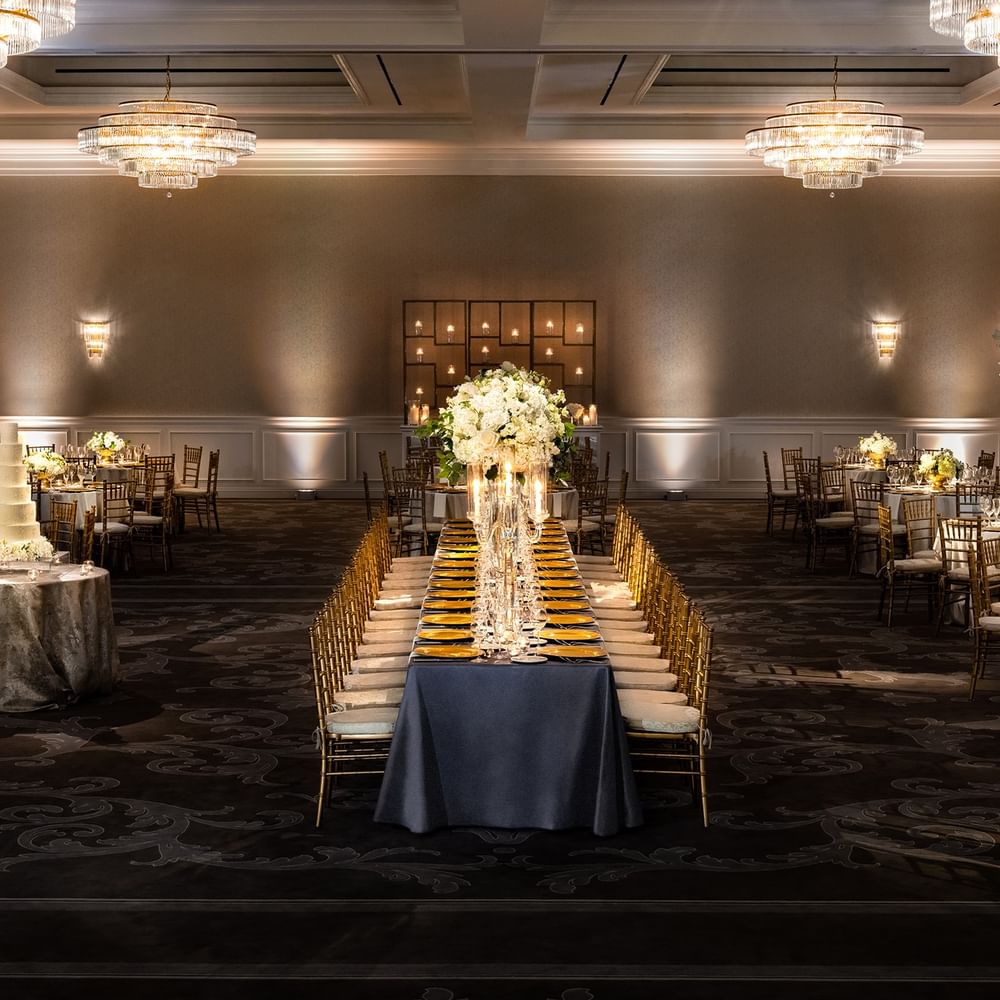 Long banquet table by gold chairs under tiered crystal chandeliers in Turtle Creek Ballroom at Warwick Melrose Dallas
