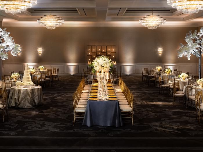 Long banquet table by gold chairs under tiered crystal chandeliers in Turtle Creek Ballroom at Warwick Melrose Dallas