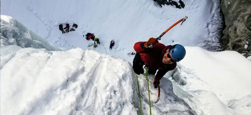 Ice climber scaling a frozen wall with ropes and gear.