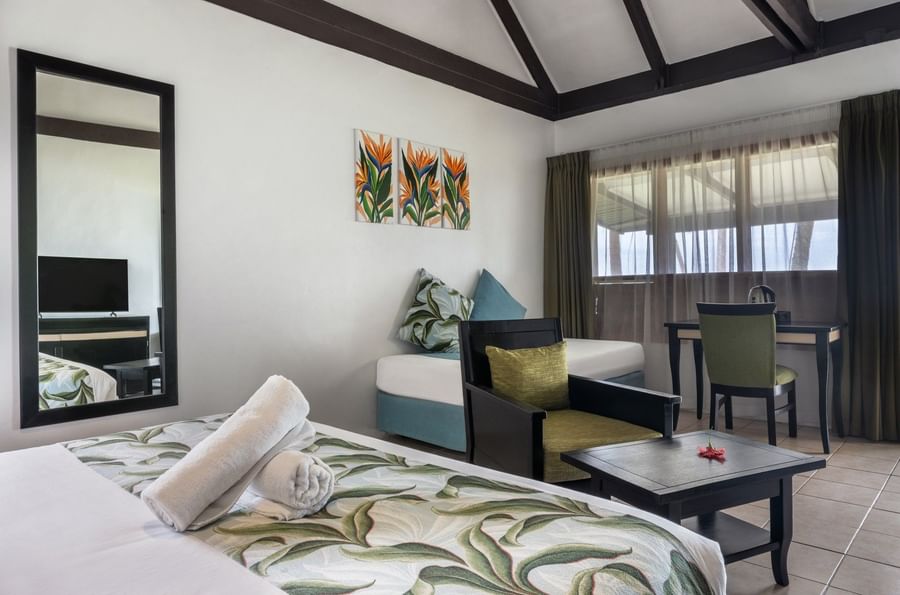 Plush bed by a black armchair and wooden desk under a vaulted ceiling in Ocean View Villa at Tambua Sands Beach Resort