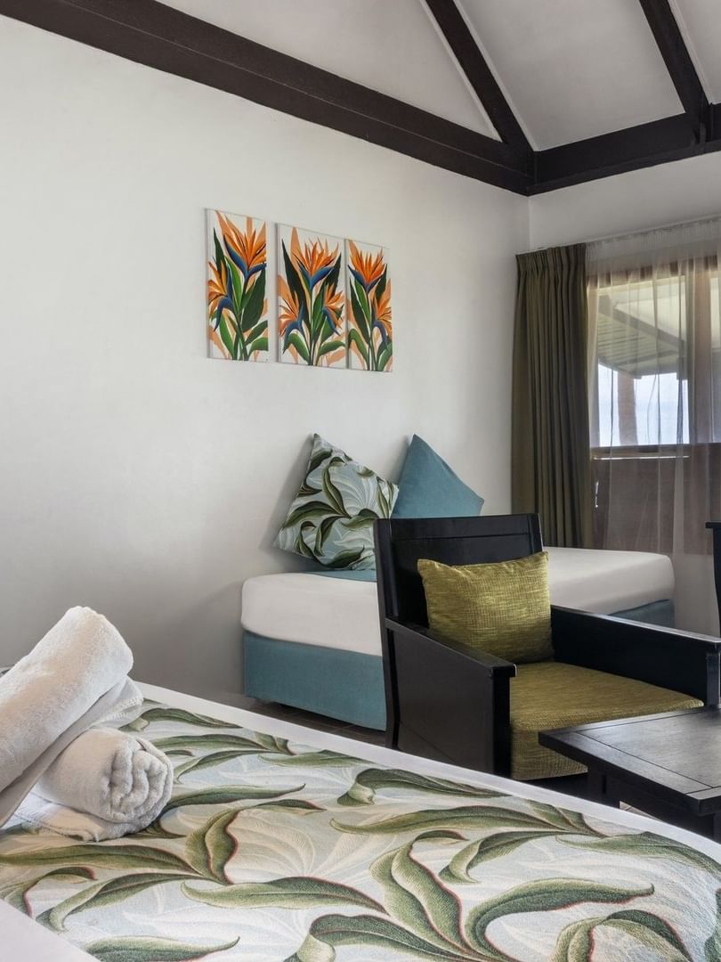 Plush bed by a black armchair and wooden desk under a vaulted ceiling in Ocean View Villa at Tambua Sands Beach Resort