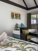 Plush bed by a black armchair and wooden desk under a vaulted ceiling in Ocean View Villa at Tambua Sands Beach Resort