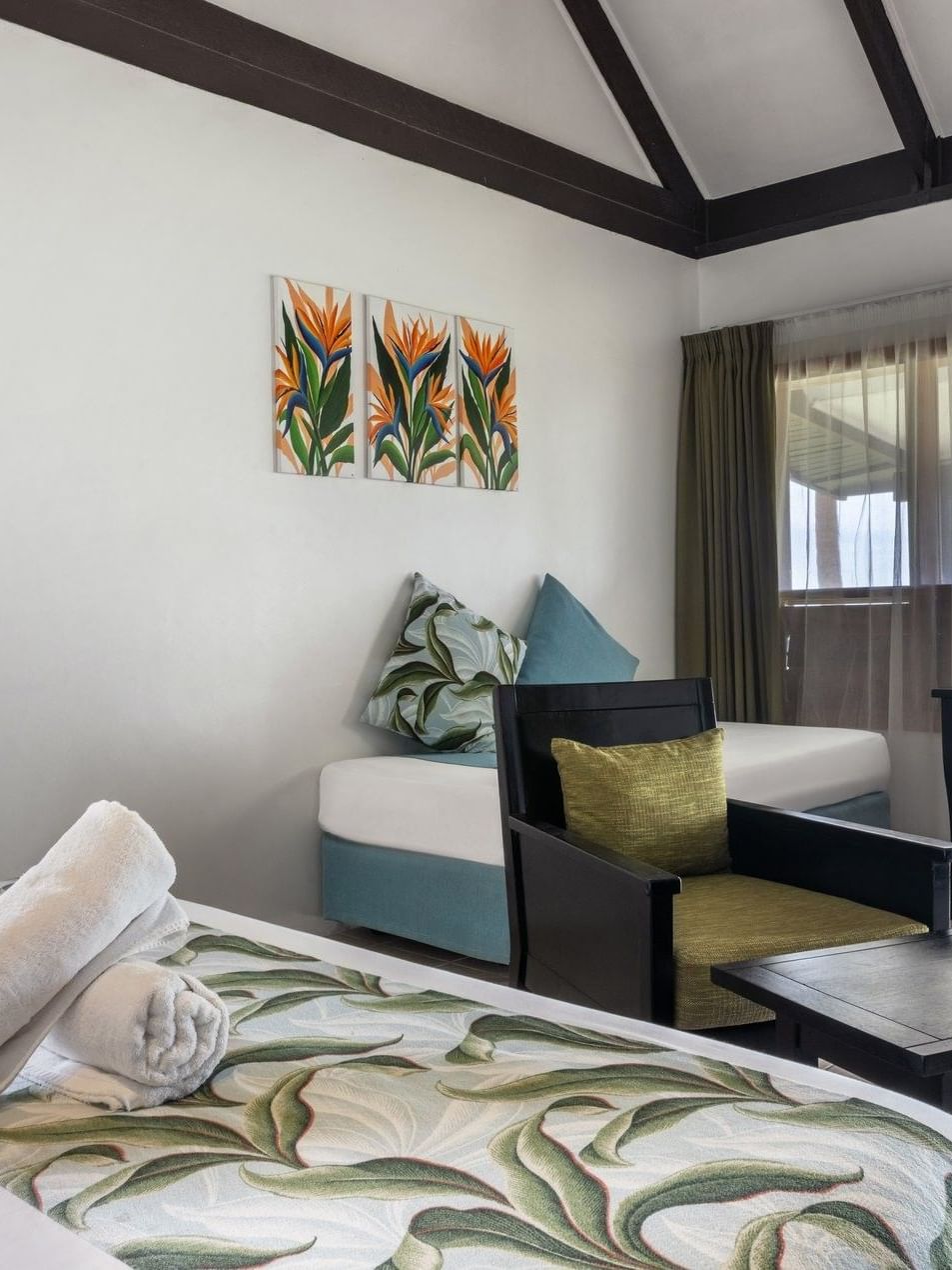 Plush bed by a black armchair and wooden desk under a vaulted ceiling in Ocean View Villa at Tambua Sands Beach Resort