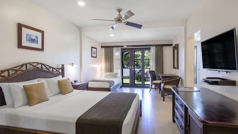 Garden view room featuring large bed facing wall-mounted TV with single bed beside seating area at warwick le lagon-vanuatu