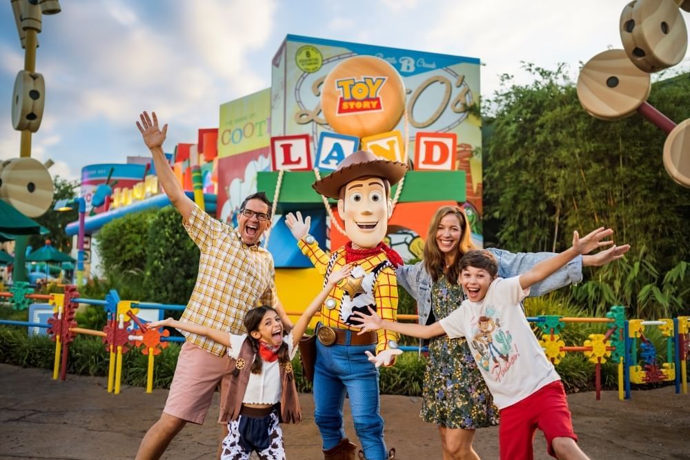 A man, woman, boy, and girl pose with Woody from Toy Story with their arms outstretched, smiling. 