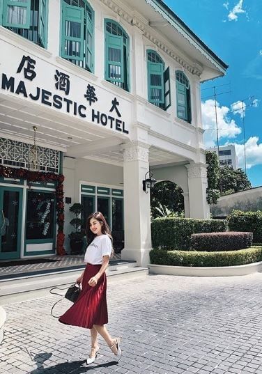 A woman in a white t-shirt and red skirt strolls past the Majestic Hotel, with elegant architecture against the blue sky