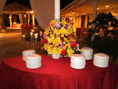 Stacked white plates by a candelabra and a floral centerpiece on a red table in Acajou Room at Hotel Montana Haiti