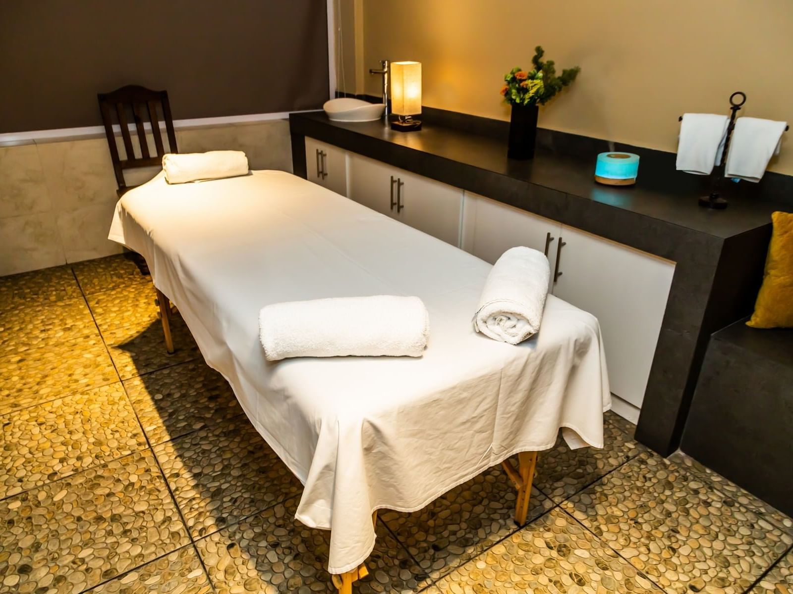 Spa bed with towels, counter-top with a lamp, washbasin & fresh flowers in Gamma Puebla Señorial Centro