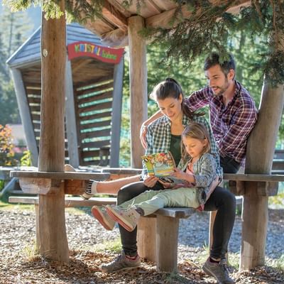 A kid with parents reading a story book at Falkensteiner Hotels