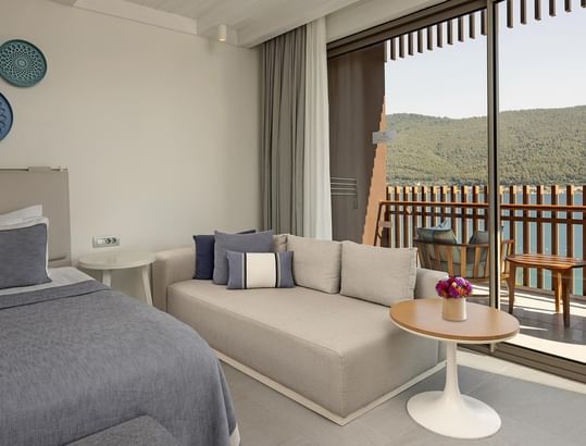 Standard Sea View Room with bed, sofa, and balcony overlooking a scenic view of sea and mountains.