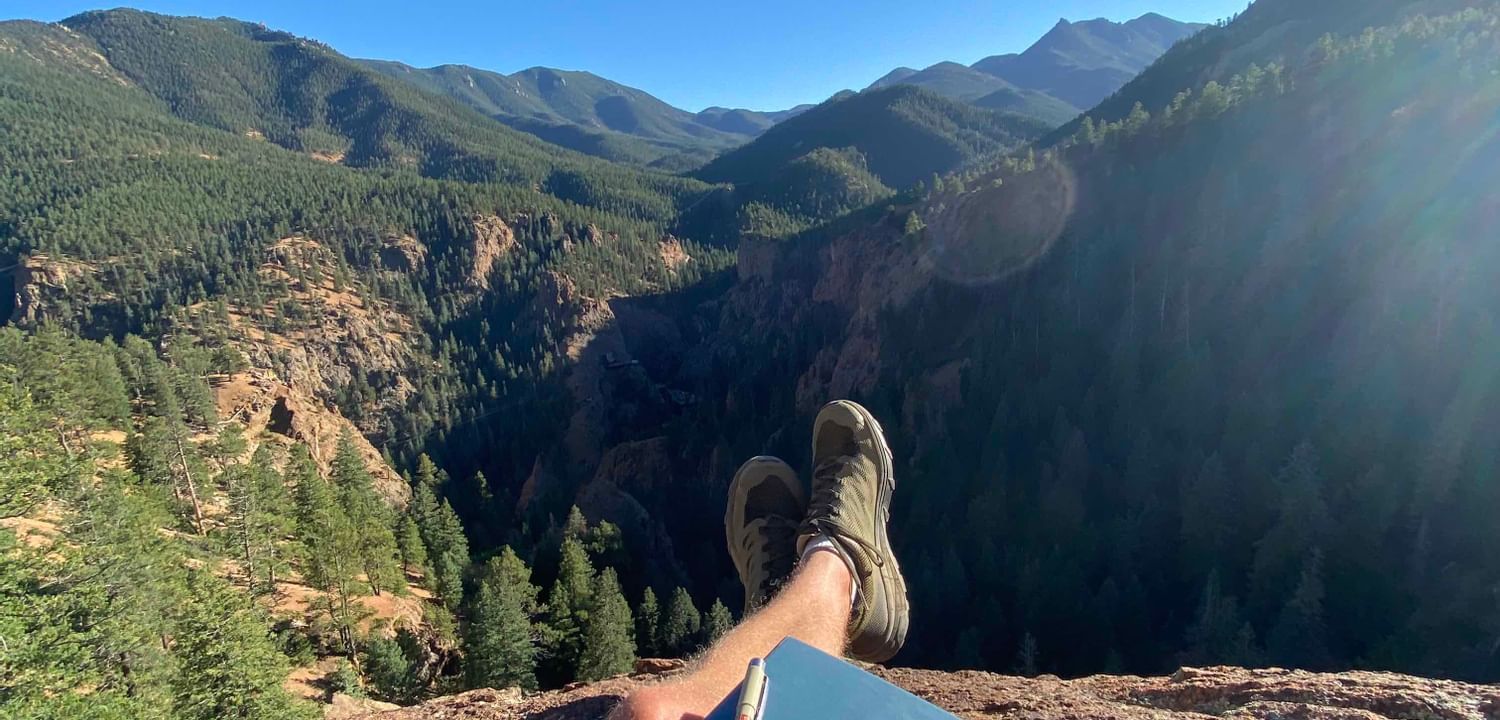 Man sitting on a mountain top with a book near Kinship Landing