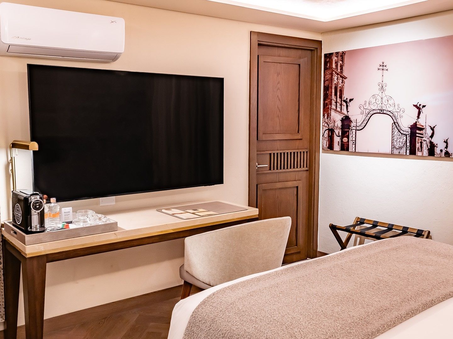 Hotel room desk with a large wall-mounted TV, coffee station, and a framed art piece in Queen Novicia at Quinta Real Puebla