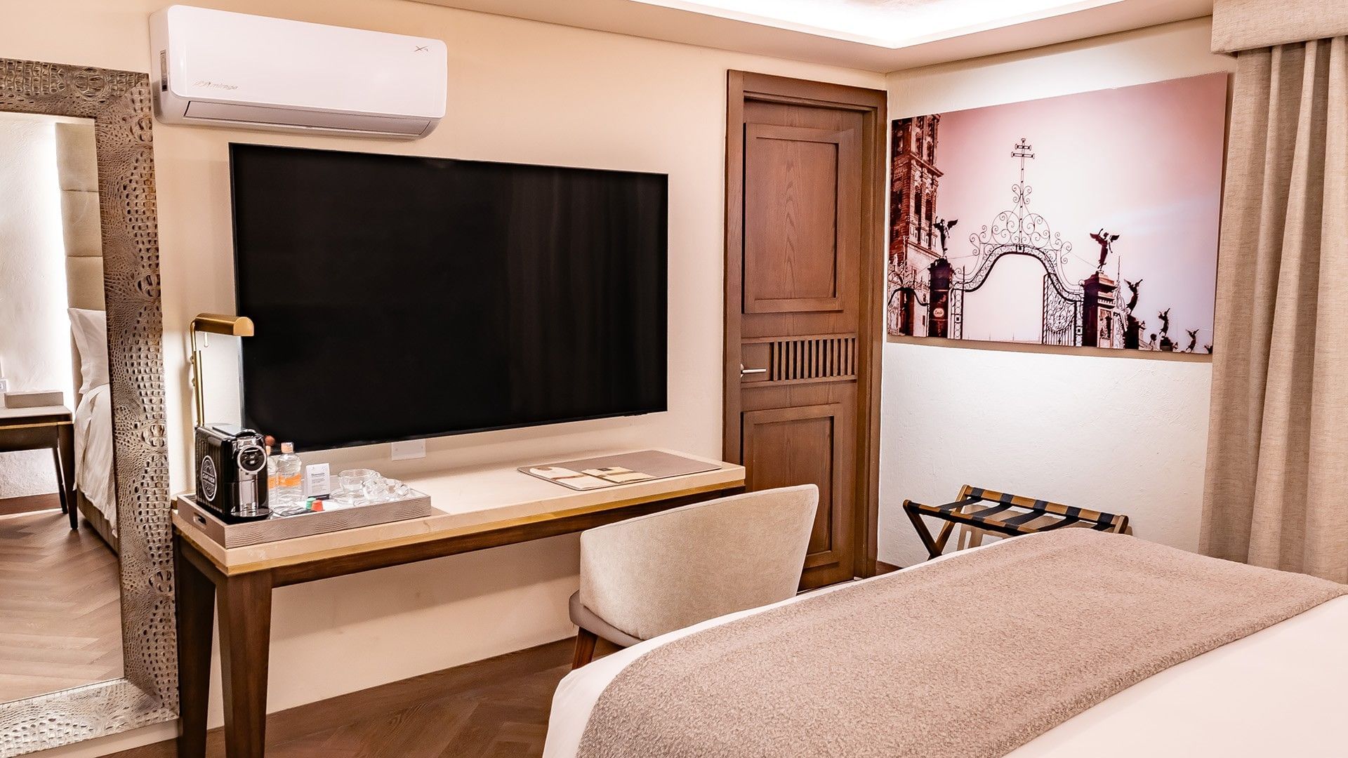 Hotel room desk with a large wall-mounted TV, coffee station, and a framed art piece in Queen Novicia at Quinta Real Puebla