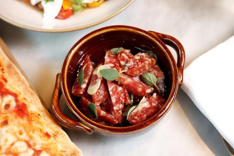 Small brown bowl filled with sliced salami, garnished with fresh herbs at the family dinner in Park Hyatt Saigon