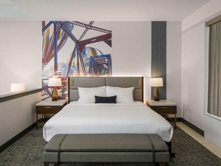 Longitude Suite featuring a king bed, a stylish gray bench, and a vibrant bridge mural at Hotel 43 Boise