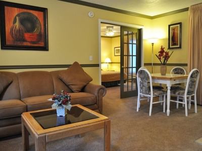 Deluxe One Bedroom Suite showing the living room couch, dining table, and bedroom through doors at Americana Village Suites