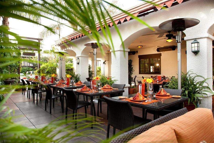 A series of tables and chairs on an outdoor patio with heating lamps and plants.