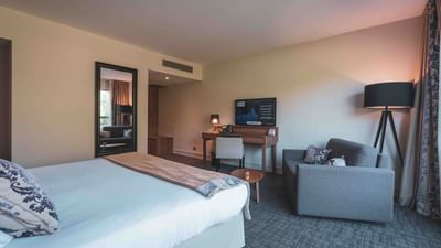Modern hotel room with large bed, couch, desk and standing lamp.